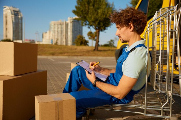 professional male courier checking document delivery before handed customer while sitting outdoors nearby cargo van 266732 36626